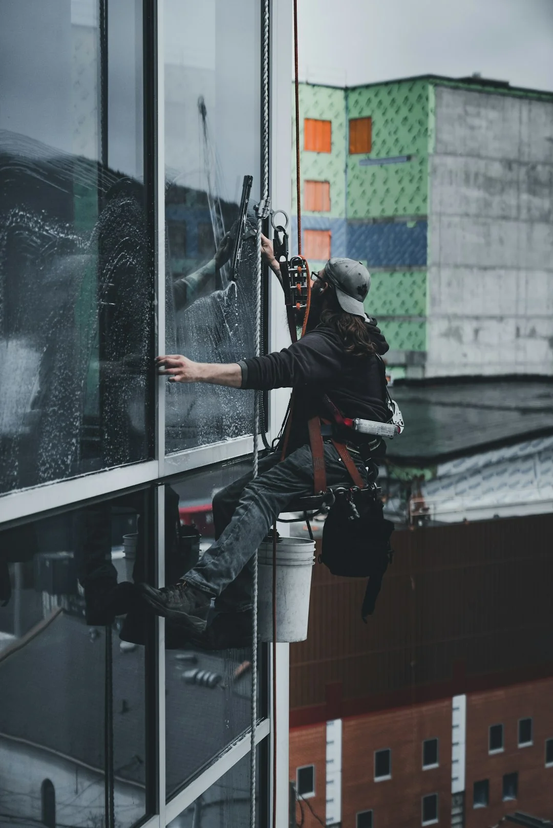 Two workers clean windows on a sleek, modern glass building facade from a suspended platform.